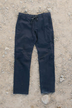 A pair of 686 Men's Everywhere® Pant - Slim Fit in black lies flat on rocky, sandy ground, shown with both legs extended and the waistband visible.