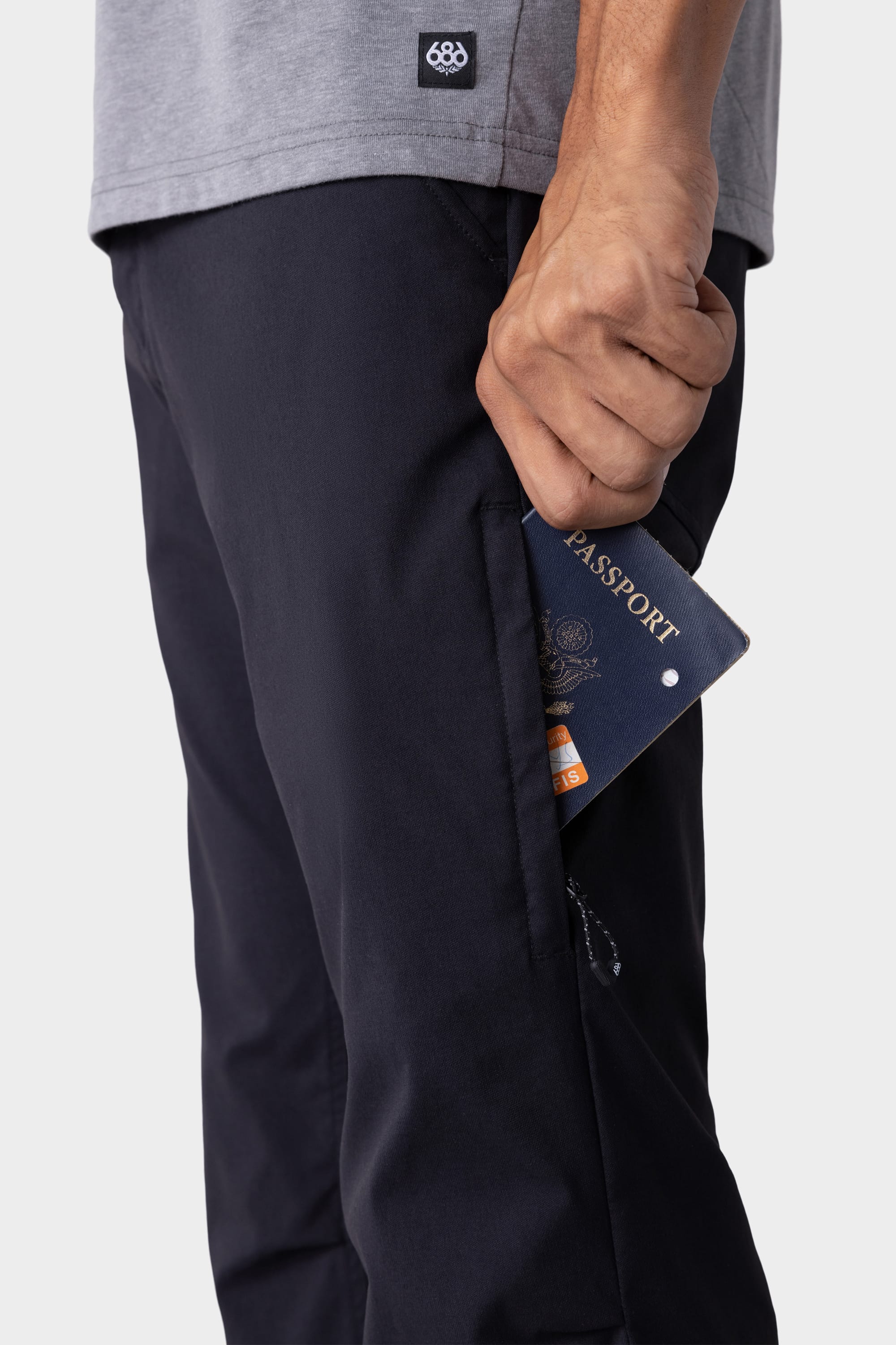Wearing 686 Men's Everywhere® Pant - Slim Fit, a person in a gray shirt slides a passport and card into the side pocket. The cropped image highlights the hand, pocket, and passport.