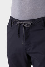 A close-up of a person wearing 686 Men's Everywhere® Pant - Slim Fit in dark navy with a gray shirt. The breathable pants show a bow-tied drawstring at the waist and belt loops around the waistband.