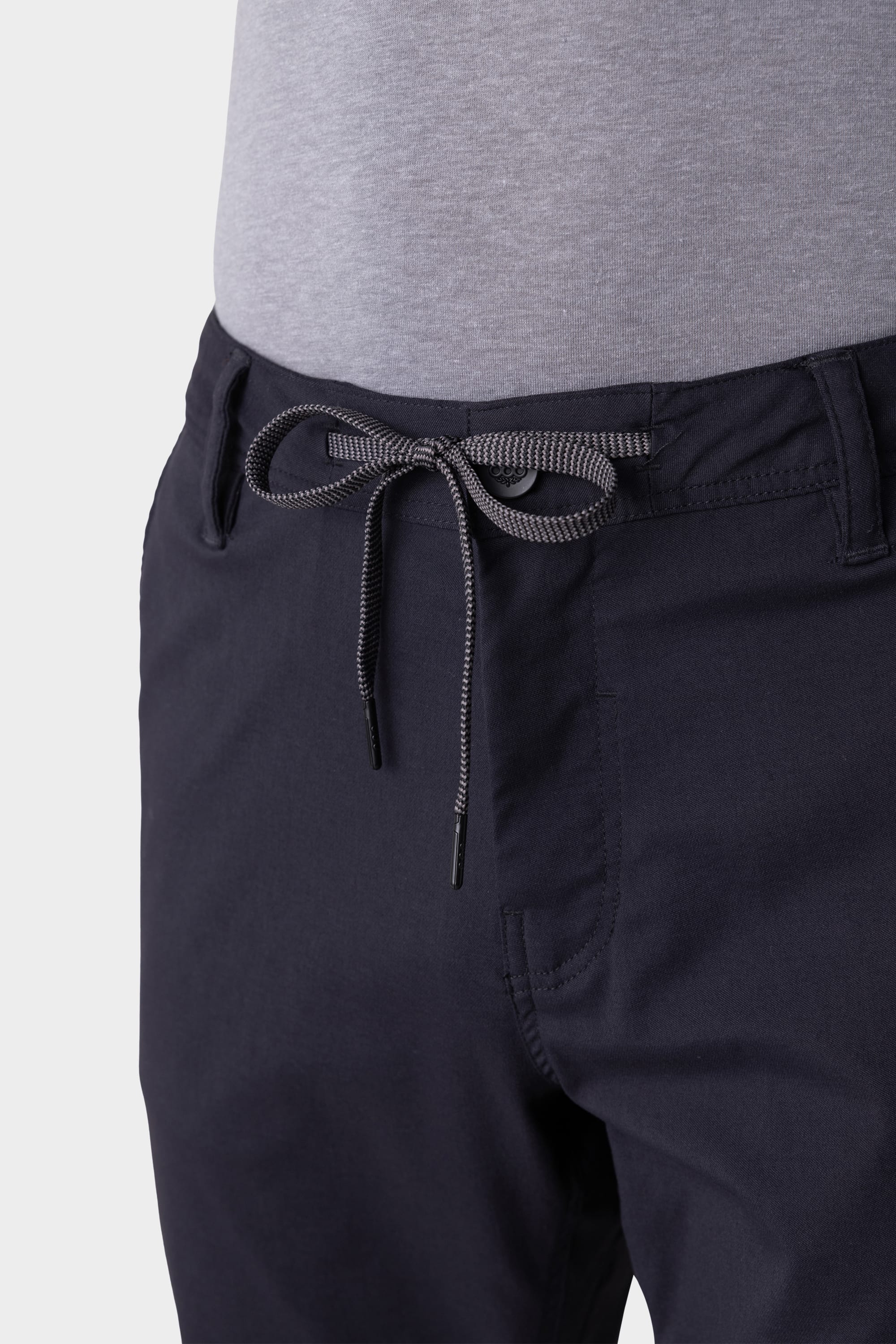 A close-up of a person wearing 686 Men's Everywhere® Pant - Slim Fit in dark navy with a gray shirt. The breathable pants show a bow-tied drawstring at the waist and belt loops around the waistband.