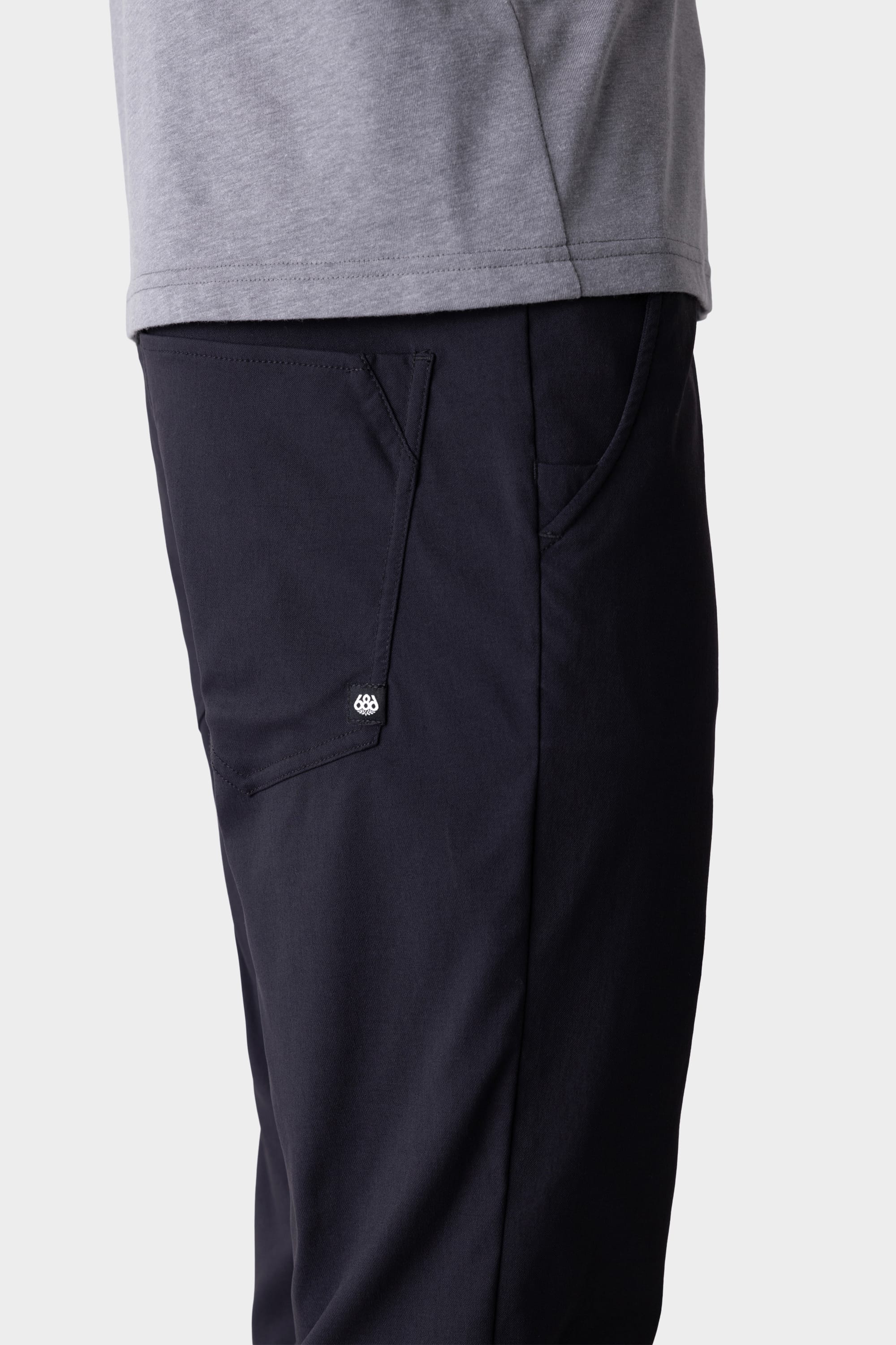 A person wearing 686 Men's Everywhere® Pant - Slim Fit in dark navy, featuring a visible side pocket and button, shown waist down against a plain background.