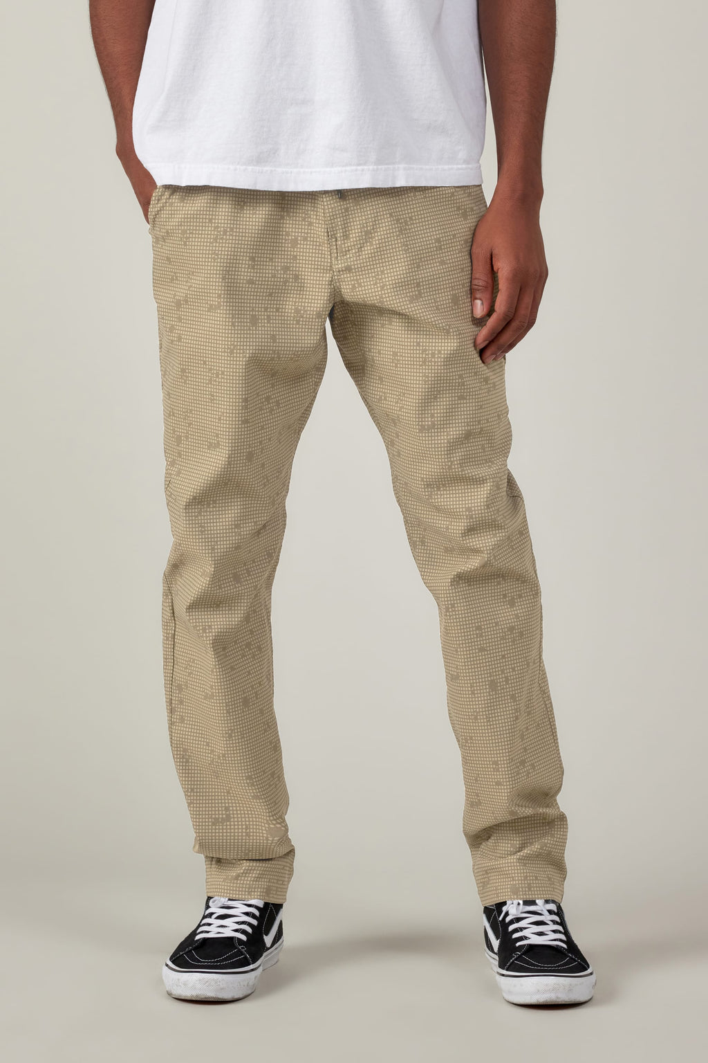 A person in a white T-shirt, 686 Men's Everywhere® Pant - Slim Fit by 686, and black-and-white sneakers stands with hands in pockets against a plain background.