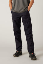 A person wearing a grey t-shirt, 686 Men's Anything Cargo Pant - Relaxed Fit by 686, and black hiking shoes stands with hands in pockets, facing forward against a plain light background.