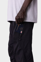 A person wearing a white shirt and 686 Men's Anything Cargo Pant - Relaxed Fit holds a passport partly tucked into a zippered side pocket. The close-up photo highlights the hand and pocket area against a plain background.