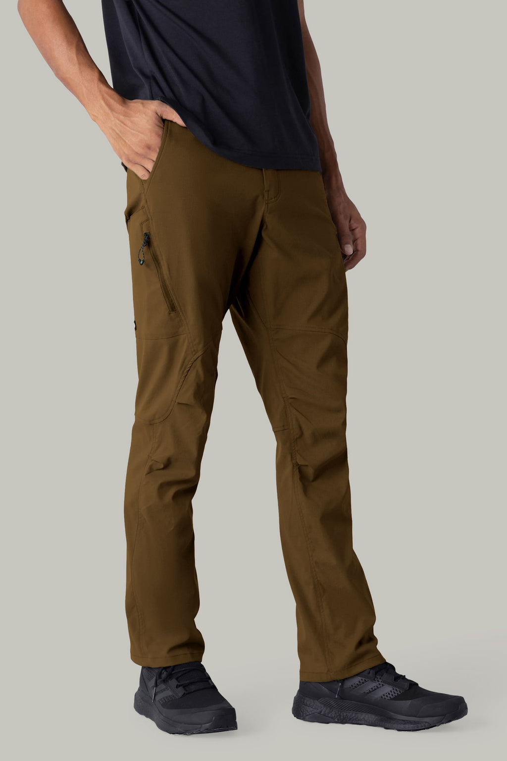 A person models the 686 Men's Anything Cargo Pant - Relaxed Fit from 686, shown from the waist down against a plain background. They're wearing black sneakers and a t-shirt, with one hand in a zippered pocket of the brown cargo pants.