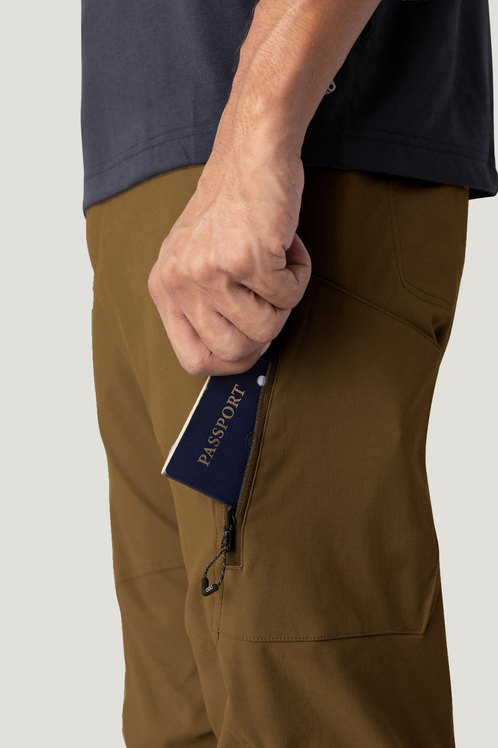 Wearing 686 Men's Anything Cargo Pant - Relaxed Fit by 686 in brown, a person with a dark shirt holds a navy blue passport partially inside the pants’ zippered side pocket.