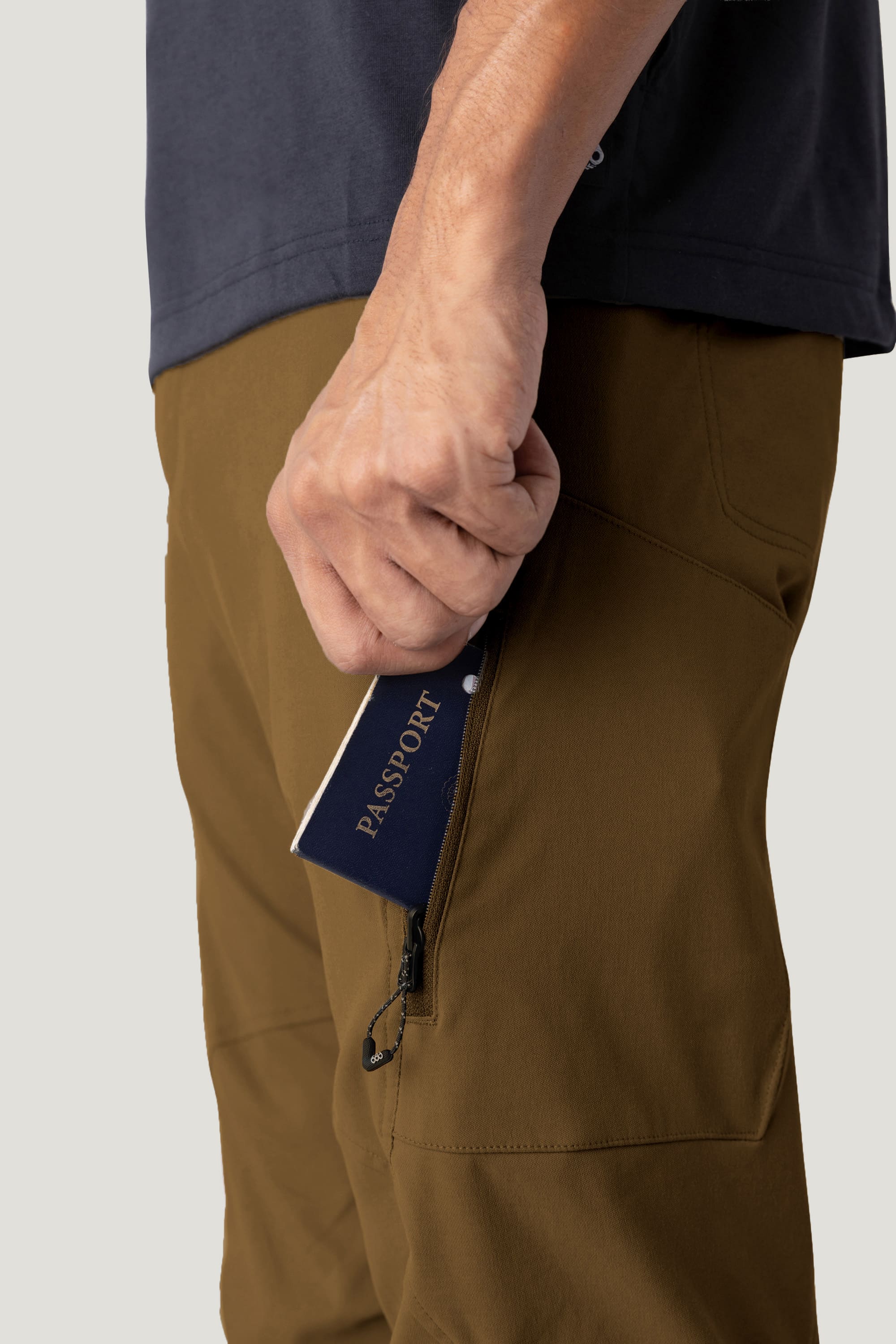 Wearing 686 Men's Anything Cargo Pant - Relaxed Fit by 686 in brown, a person with a dark shirt holds a navy blue passport partially inside the pants’ zippered side pocket.