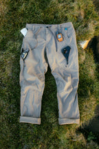 The 686 Men's Anything Cargo Pant - Relaxed Fit by 686 is shown lying on grass, with articulated knees and gadgets like a phone, GPS unit, and notepad visible in its pockets.