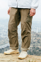 A person stands on a rocky ledge in 686 Men's Anything Cargo Pant - Relaxed Fit by 686, styled with white shoes and a white jacket. The city and hills are blurred in the background.