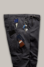 The 686 Men's Anything Cargo Pant - Relaxed Fit by 686 is shown laid flat in dark gray with 13 pockets holding a passport, wallet, smartphone, folded cash, and keys clipped to a belt loop, highlighting its organized, 4-way stretch design.