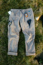 The 686 Men's Anything Cargo Pant - Relaxed Fit by 686 is shown on grass with a smartphone, GPS device, and small electronics organized in its multiple 4-way stretch pockets and waistband.