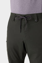 A close-up of a person wearing the 686 Men's Anything Cargo Pant - Relaxed Fit in dark green, featuring a black and white drawstring, belt loops, zipper fly, and 4-way stretch, paired with a light purple or gray shirt. Brand: 686.