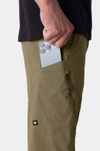 A person wearing 686 Men's Anything Cargo Pant - Relaxed Fit in olive green and a black shirt puts a smartphone into the pants’ zippered side pocket.