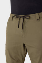 A close-up shows a person wearing the 686 Men's Anything Cargo Pant - Relaxed Fit in olive green with a black drawstring at the waist, paired with a black shirt. The image highlights the 686 waistband and upper thigh area.