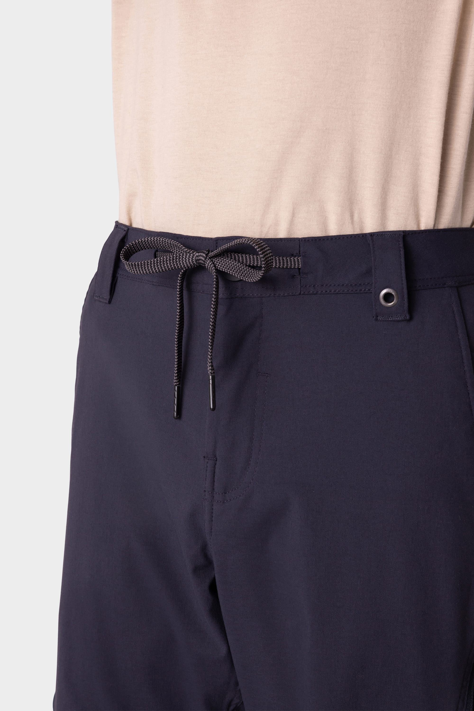A close-up of a person wearing 686 Men's Anything Cargo Pant - Relaxed Fit in navy blue with a gray drawstring waist, paired with a tucked-in beige shirt.