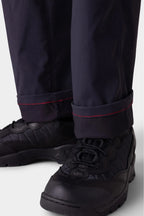Close-up of a person wearing 686 Men's Anything Cargo Pant - Relaxed Fit by 686 in black, featuring red cuff stitching and paired with black lace-up athletic shoes. The pants are slightly rolled up to highlight the red stitching detail.
