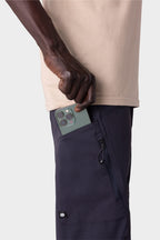 A person in a beige shirt and 686 Men's Anything Cargo Pant - Relaxed Fit by 686 puts a green smartphone with three cameras into the zippered pocket of their 4-way stretch cargo pants.