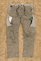 The 686 Men's Anything Cargo Pant - Relaxed Fit from 686, featuring a camouflage pattern and 13 pockets, rests on dirt with a phone and utility tool in the pockets and drawstrings visible at the waist.