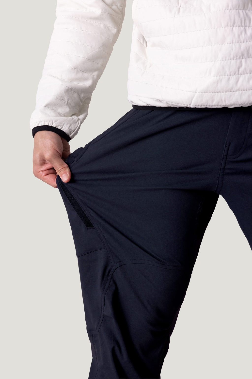 A person in a white jacket stretches the fabric of their black 686 Men's Anything Cargo Pant - Relaxed Fit with one hand, showing off the flexibility of these 686 cargo pants.