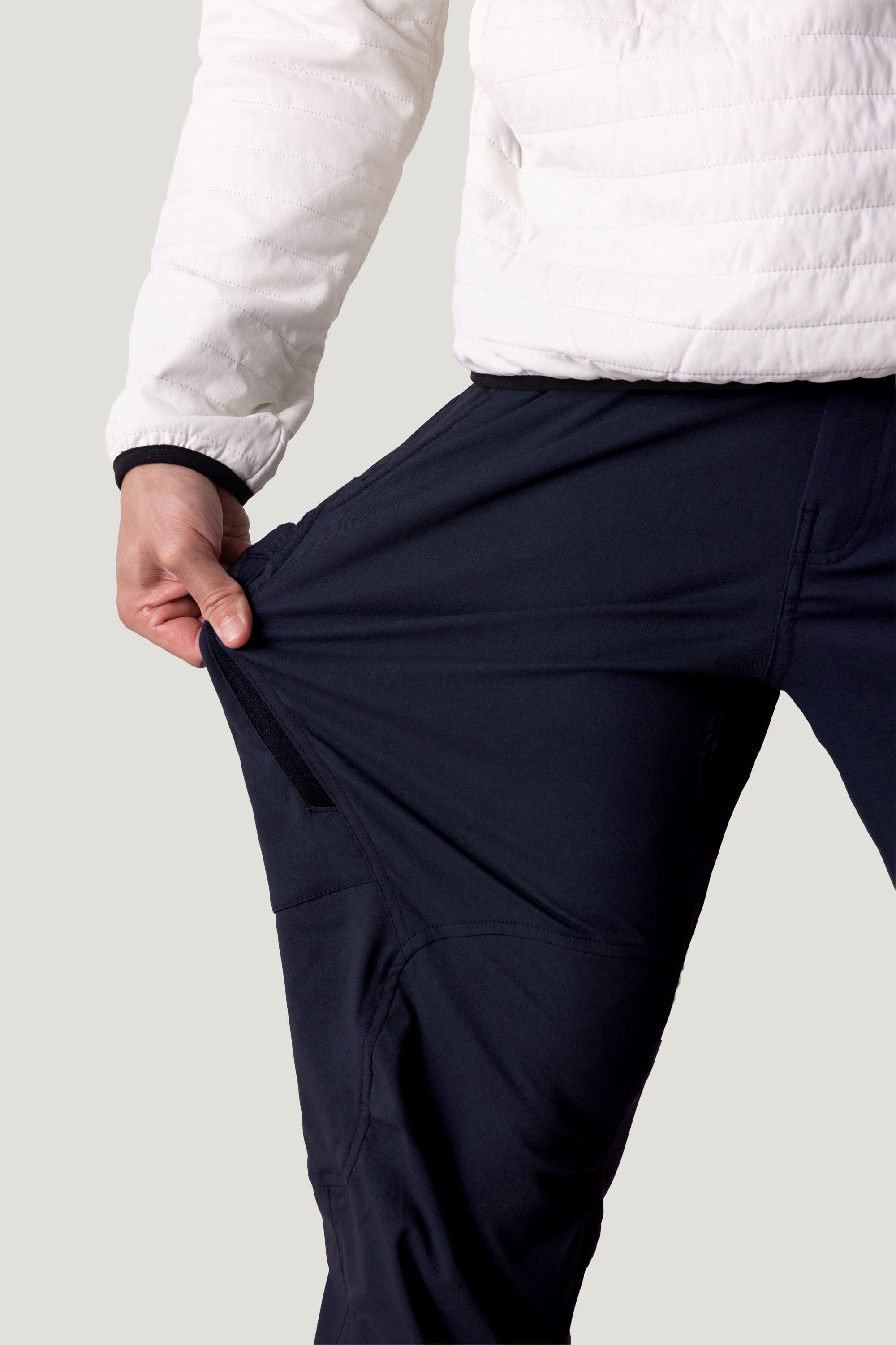 A person in a white jacket stretches the fabric of their black 686 Men's Anything Cargo Pant - Relaxed Fit with one hand, showing off the flexibility of these 686 cargo pants.