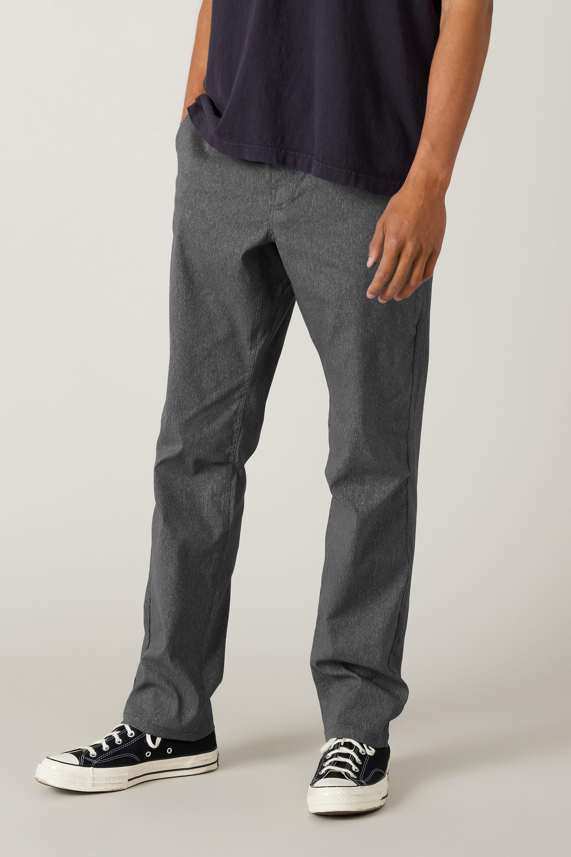 A person wearing a dark short-sleeve shirt, 686 Men's Everywhere® Pant - Relaxed Fit by 686, and black-and-white sneakers stands against a plain light background, with their left hand resting near their pocket.
