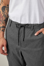 A person wears a white t-shirt and 686 Men's Everywhere® Pant - Relaxed Fit in gray by 686, with one hand in their pocket. The breathable pants highlight their tattooed arm and thin bracelet for an effortlessly cool look.