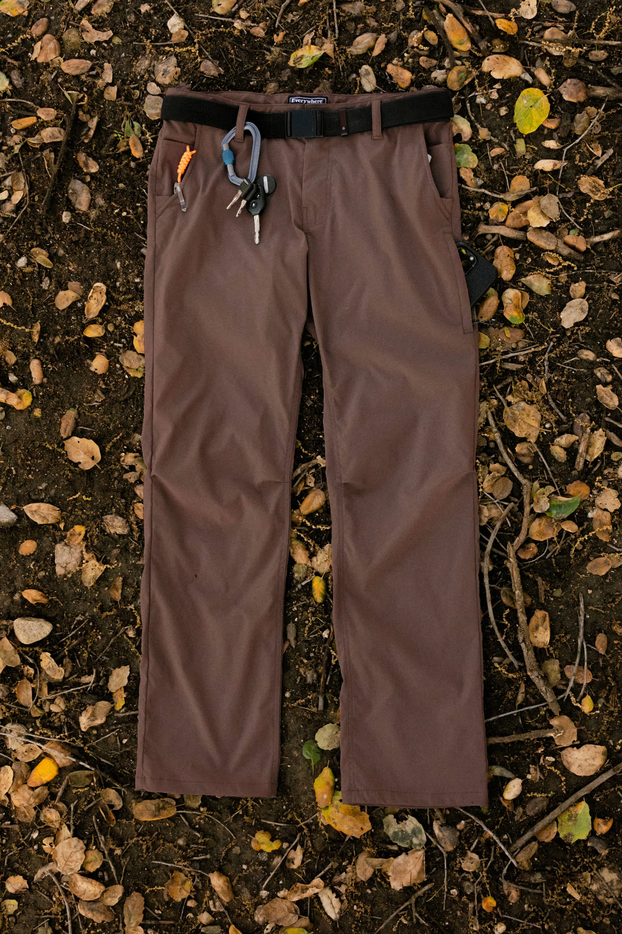 The 686 Men's Everywhere® Pant - Relaxed Fit by 686 features breathable fabric, a black belt, orange and blue carabiners, and keys on the belt loops—perfectly stain-resistant for outdoor adventures among yellow and brown leaves.