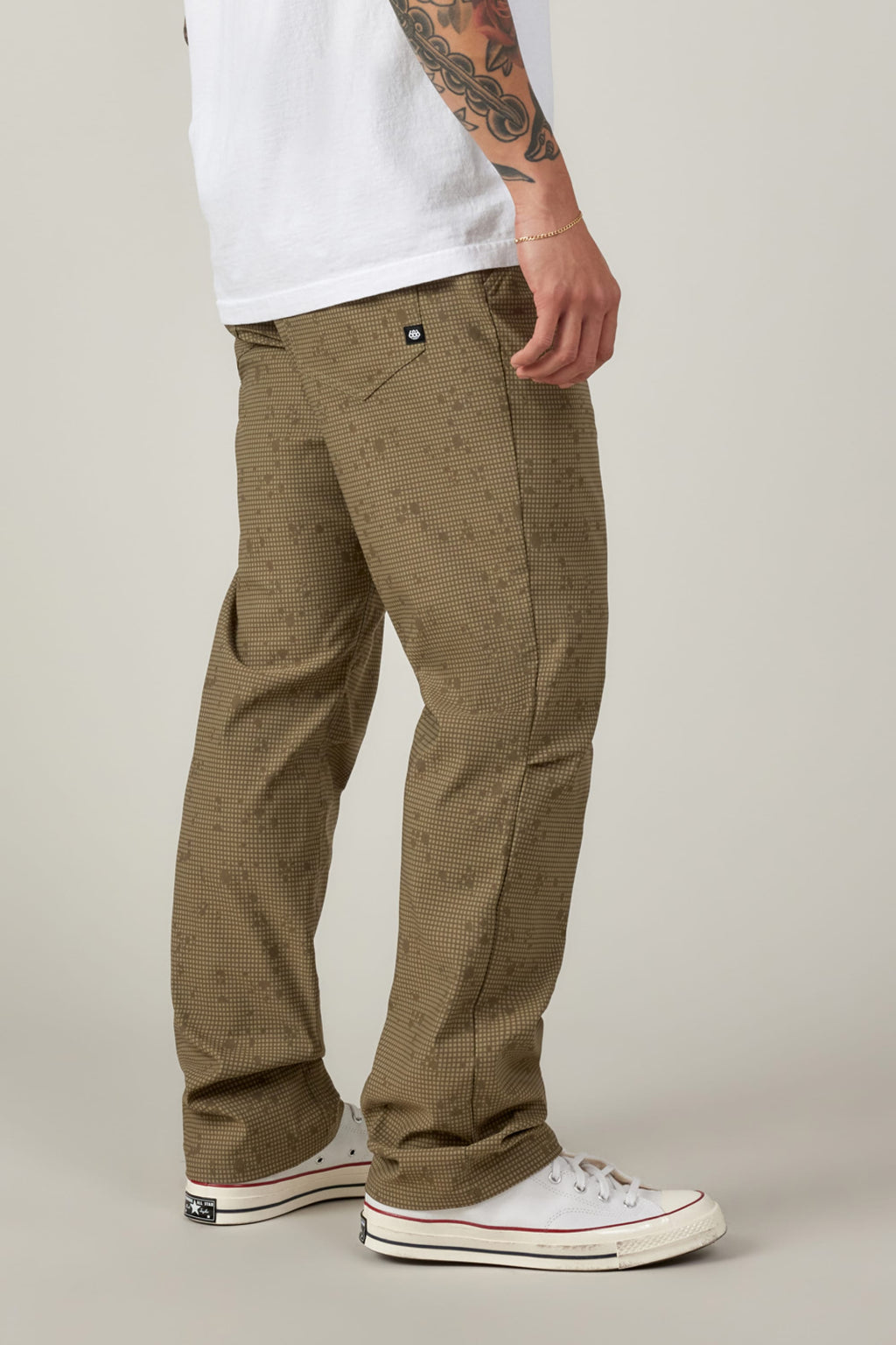 A person stands sideways in 686 Men's Everywhere® Pant - Relaxed Fit and a white tee with visible tattoo sleeve, sporting white sneakers against a neutral background.