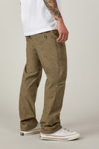 A person stands sideways in 686 Men's Everywhere® Pant - Relaxed Fit and a white tee with visible tattoo sleeve, sporting white sneakers against a neutral background.