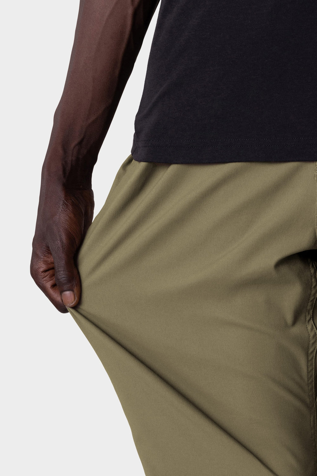 A person wearing the 686 Men's Everywhere® Pant - Relaxed Fit in olive green stretches the fabric with their left hand, showing its flexible, stain-resistant material.