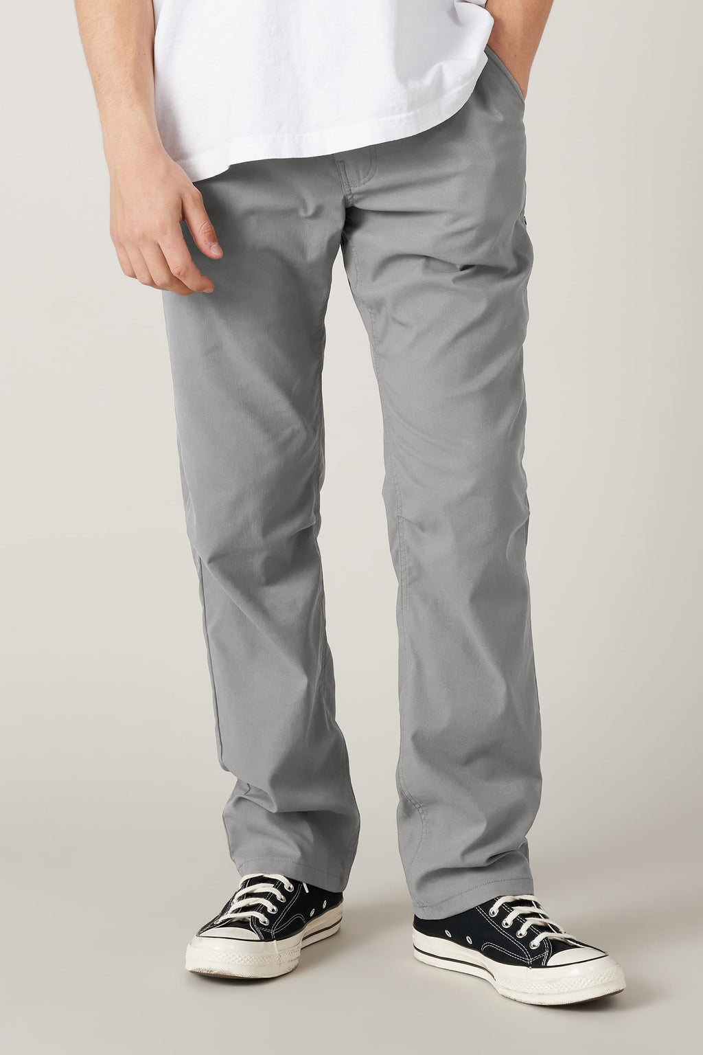 A person wearing the 686 Men's Everywhere® Pant - Relaxed Fit in light gray, a white T-shirt, and black low-top sneakers with white soles stands with one hand in a pocket; only their lower half is shown against a plain background.