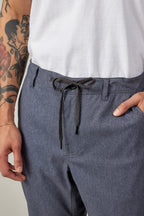 A person wears a white t-shirt and 686 Men's Everywhere® Pant - Relaxed Fit by 686 in blue, with one hand in their pocket. Their exposed arm displays a colorful tattoo featuring floral and face elements.