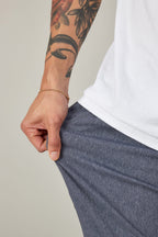 A person in 686 Men's Everywhere® Pant - Relaxed Fit stretches the fabric with one hand, revealing a floral forearm tattoo and a gold chain bracelet.