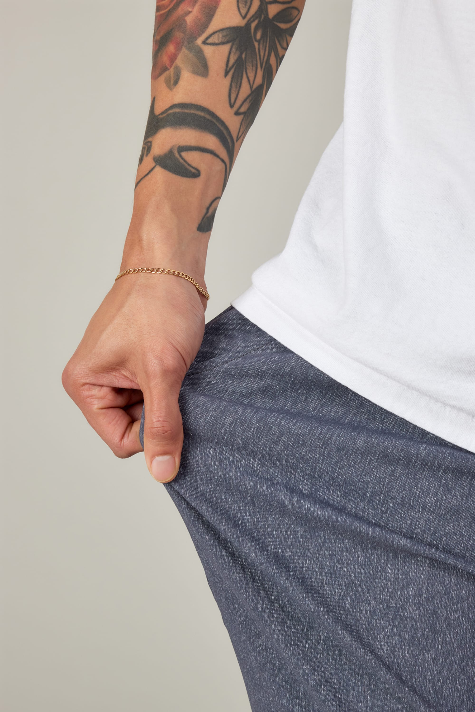 A person in 686 Men's Everywhere® Pant - Relaxed Fit stretches the fabric with one hand, revealing a floral forearm tattoo and a gold chain bracelet.