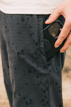 A hand places a black smartphone into the pocket of 686 Men's Everywhere® Pant - Relaxed Fit. The focus is on the hand, phone, and pocket, with a white shirt partially visible at the top.