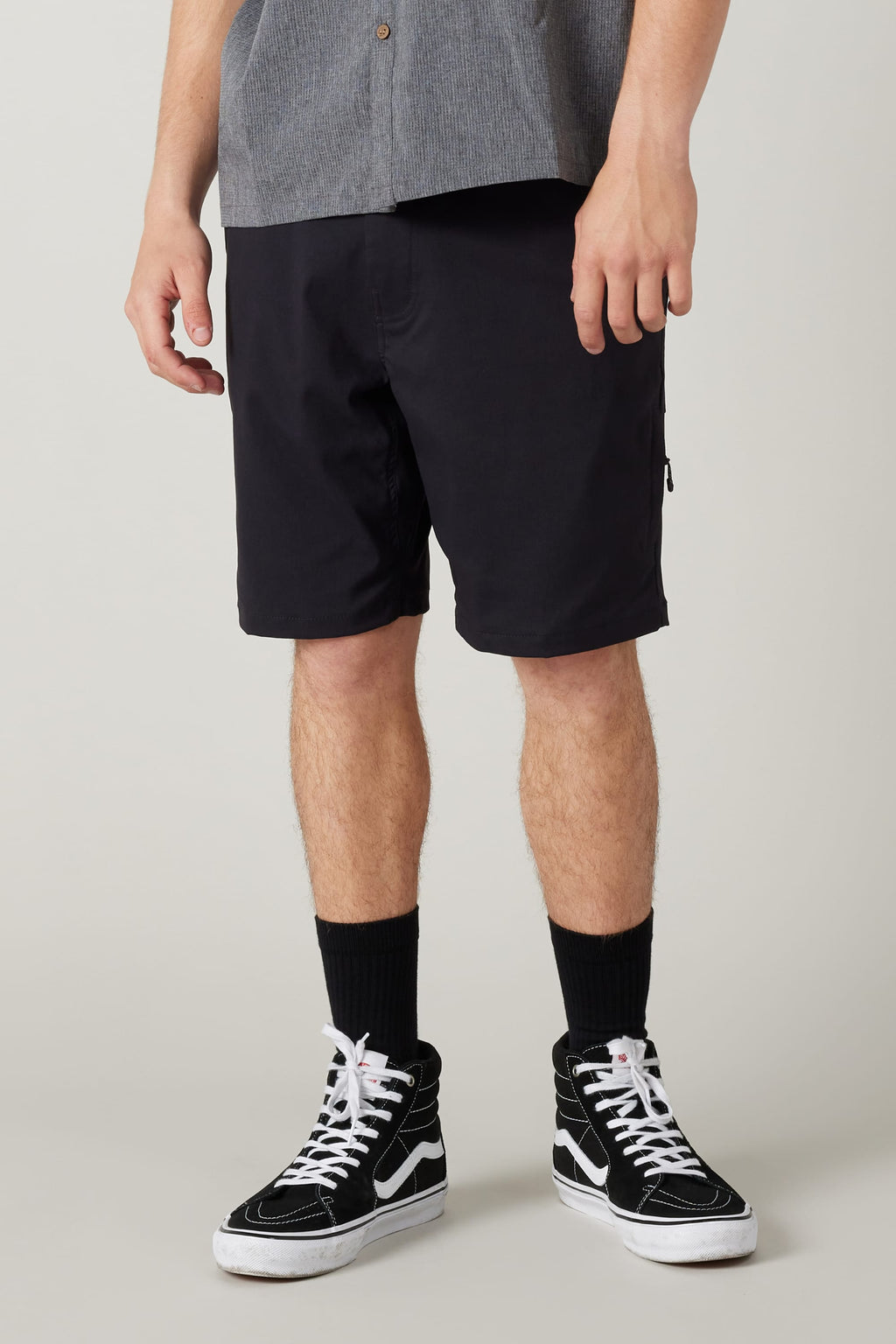 A person in a gray short-sleeve shirt, black 686 Everywhere® Hybrid Short, black crew socks, and black high-top sneakers stands against a light background. The photo is cropped at the shoulders.