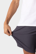 A person wearing a white shirt and dark gray 686 Everywhere® Hybrid Short stretches its fabric with their left hand to show flexibility, against a light gray background.