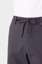 Close-up of a person wearing the 686 Everywhere® Hybrid Short in dark gray with a black drawstring at the waist, paired with a white shirt. The breathable 686 shorts are shown against a plain, light-colored background.