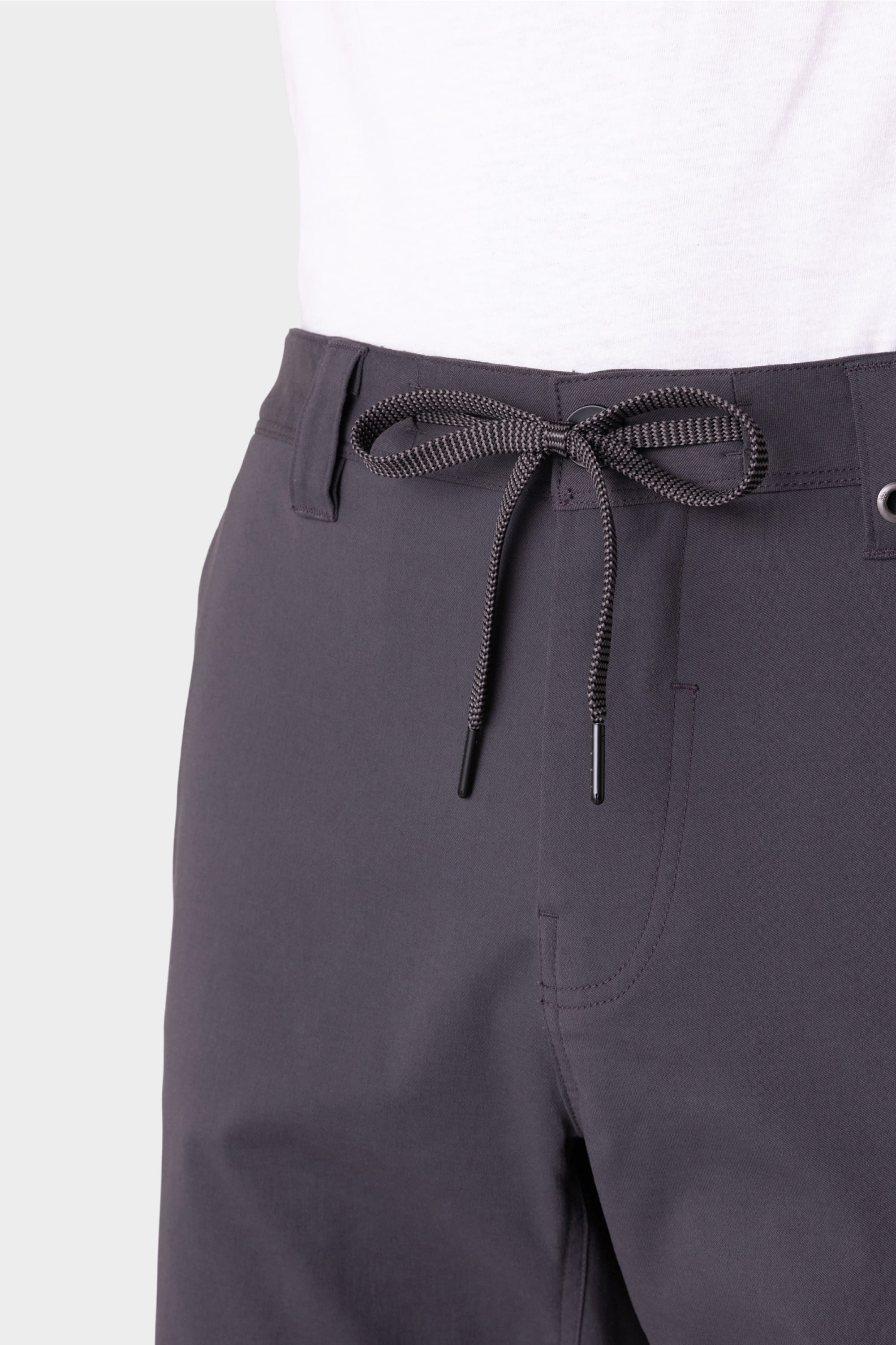 Close-up of a person wearing the 686 Everywhere® Hybrid Short in dark gray with a black drawstring at the waist, paired with a white shirt. The breathable 686 shorts are shown against a plain, light-colored background.