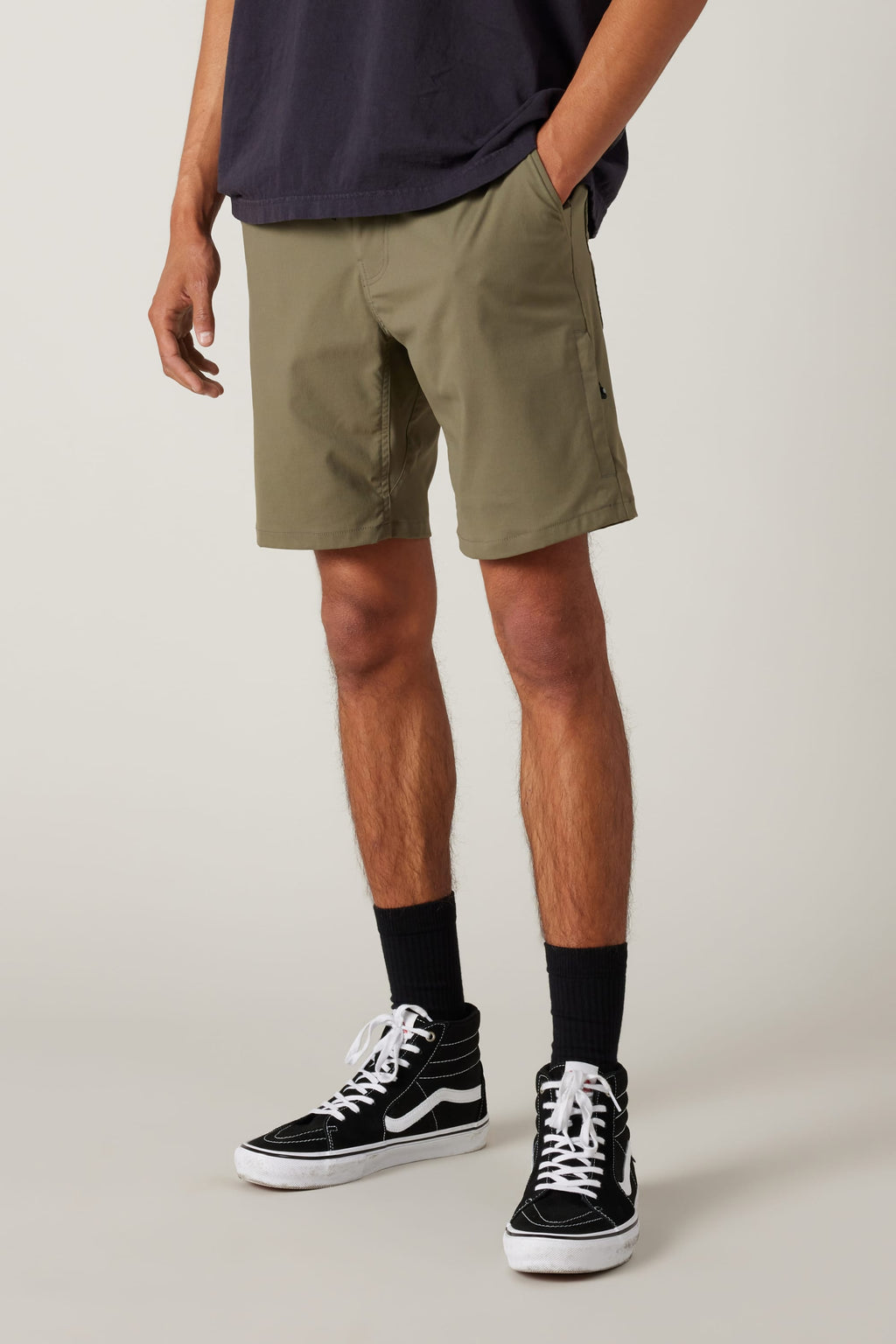 A person wears 686 Everywhere® Hybrid Shorts in olive green, paired with a dark tee, black crew socks, and black high-top sneakers. Only their lower half is shown against a light background.