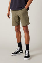 A person wears 686 Everywhere® Hybrid Shorts in olive green, paired with a dark tee, black crew socks, and black high-top sneakers. Only their lower half is shown against a light background.