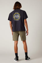 A person faces away in 686 Everywhere® Hybrid Short by 686, paired with a black tee featuring a circular logo, black socks, and black-and-white sneakers against a plain light background.