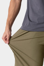 A person wearing 686 Everywhere® Hybrid Shorts in olive green stretches the fabric at the hip with one hand to show its flexibility; they also have on a gray shirt.