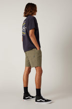 A person with medium-length hair stands sideways wearing a dark graphic T-shirt, 686 Everywhere® Hybrid Short by 686, black socks, and black Vans sneakers against a plain light background.