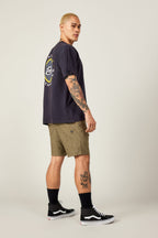 A person with short blond hair and tattoos stands in a side pose, wearing a black tee with a round back graphic, 686 Everywhere® Hybrid Short by 686, black crew socks, and black Vans sneakers.