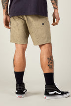 Wearing tan 686 Men's Everywhere® Hybrid Shorts, a black tee, black crew socks, and high-top sneakers, the person stands facing away. The stain-resistant shorts from 686 complement visible arm and leg tattoos.