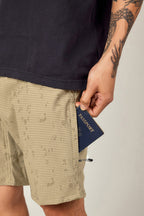 A tattooed person, dressed in 686 Men's Everywhere® Hybrid Short and a dark shirt, holds a navy blue passport partially out of their shorts pocket.