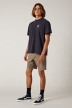 A young man with shoulder-length hair stands in a neutral pose wearing a dark t-shirt, 686 Everywhere® Hybrid Short by 686, black socks, and black sneakers with white soles against a plain light background.