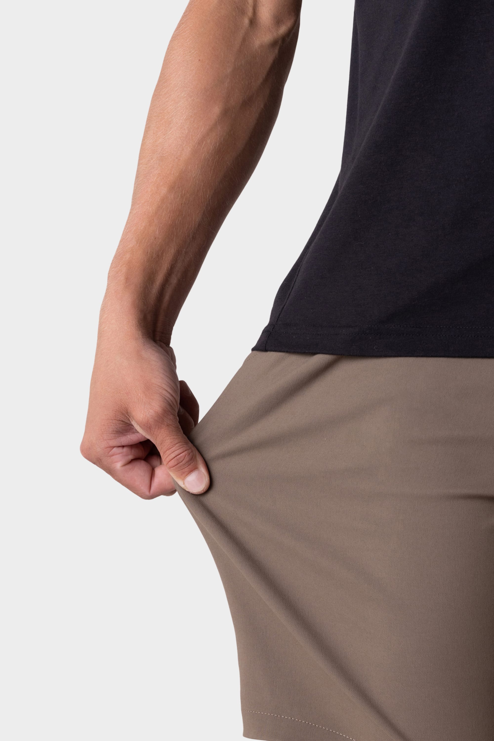 A person wearing a black shirt stretches the fabric of their 686 Everywhere® Hybrid Short with one hand, showcasing its flexibility. The background is plain white.
