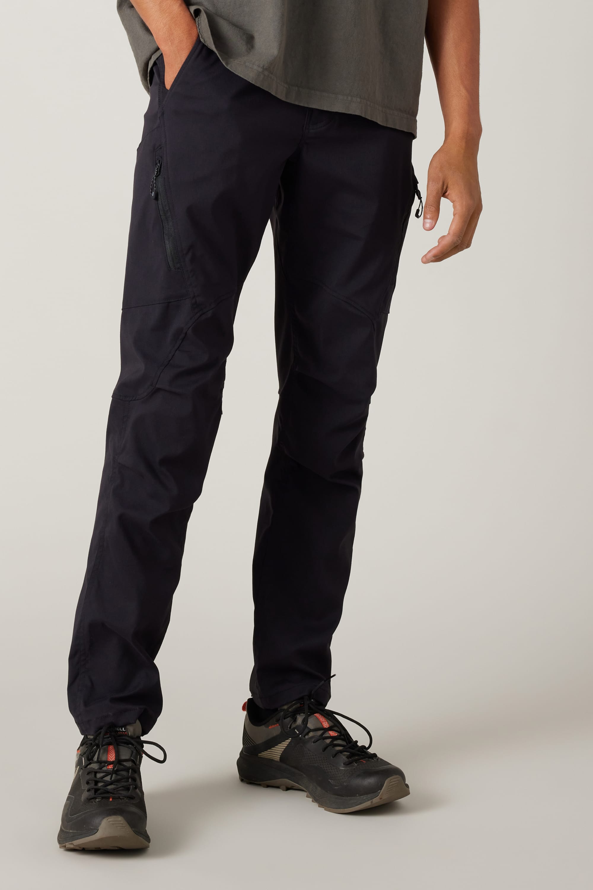 A person wears the 686 Men's Anything Cargo Pant - Slim Fit in black with black hiking shoes and a gray shirt, standing with one hand in their pocket against a light background. The photo highlights the pants, perfect for adventure.